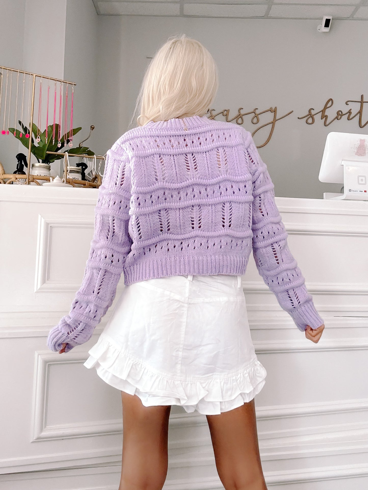 Lilac open-knit cropped cardigan, styled with a white ruffle skirt.