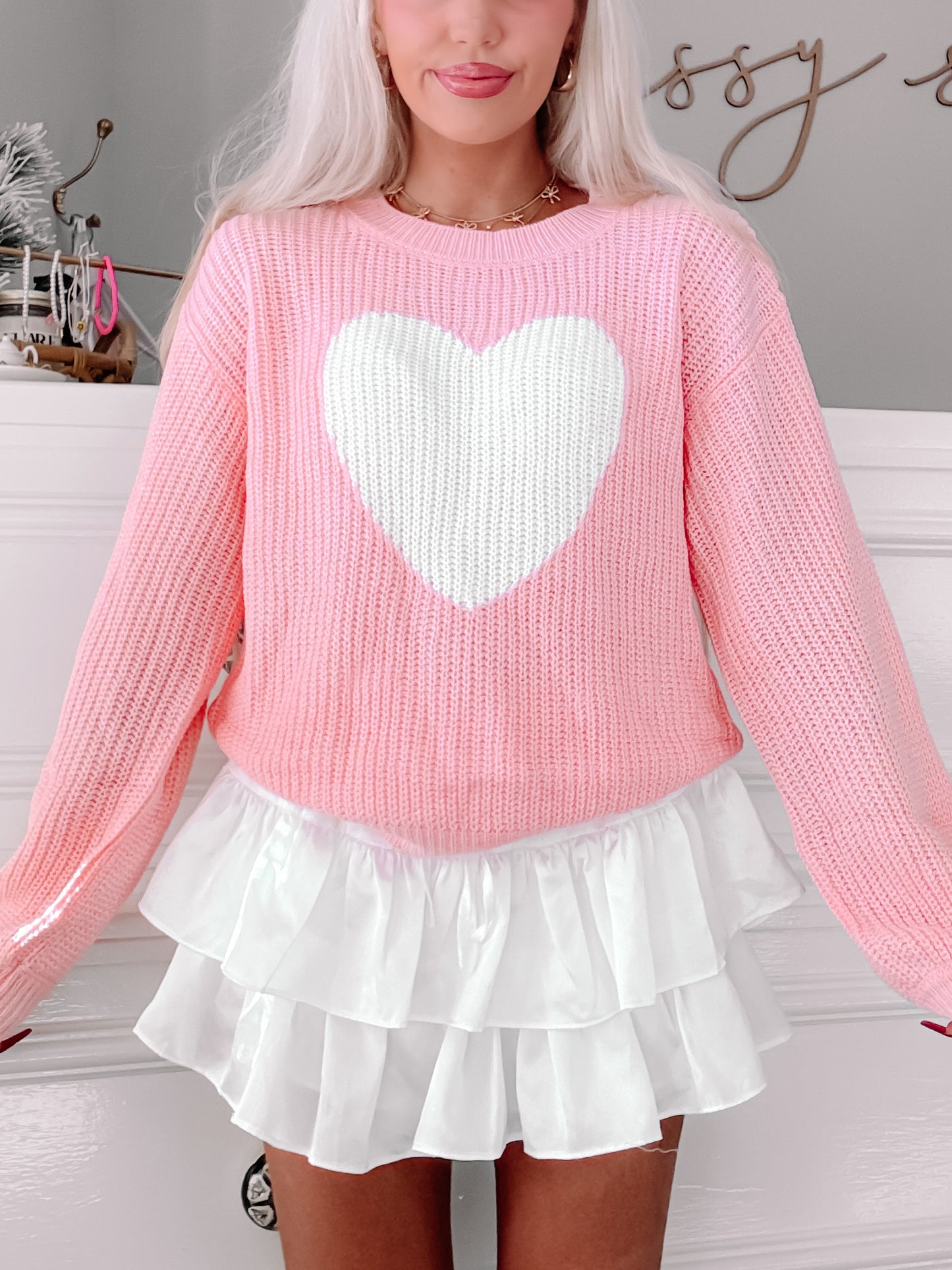 Pink knit sweater featuring a large white heart, styled with a white ruffled skirt.