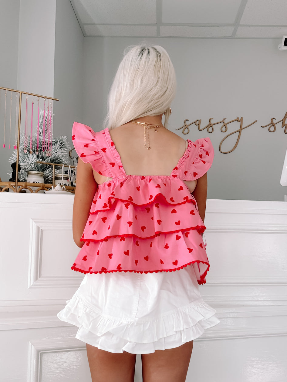 Pink tiered ruffle top with red heart print, styled with white ruffled shorts.