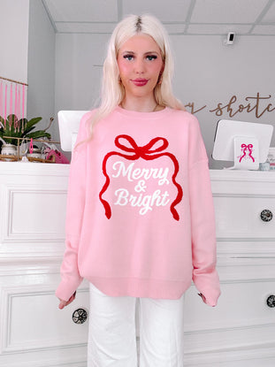 Person wearing a pink sweater with 'Merry & Bright' text in a decorative bow design from sassy shortcake