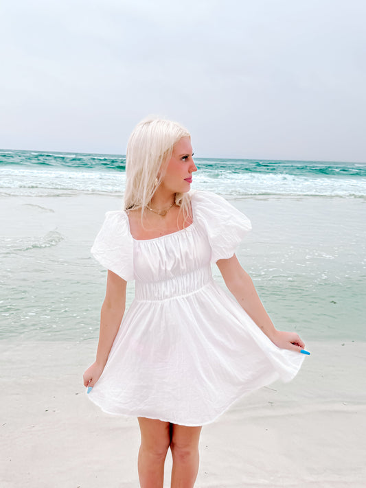 Morning Light White puff-sleeve mini dress from Sassy Shortcake white summer dress on beach, ocean backdrop.