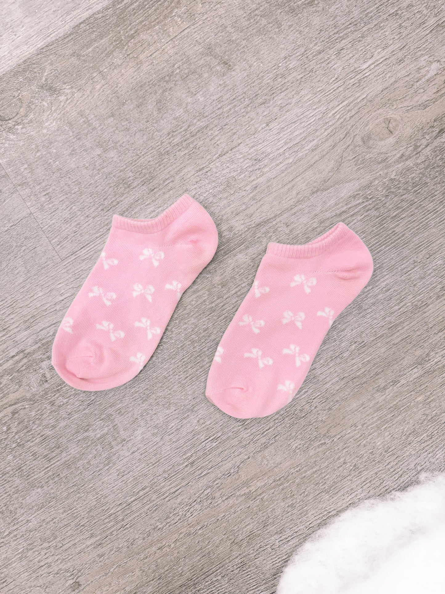 Pink ankle socks with a bow pattern, shown on a wood background.