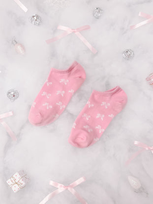Pink bow-patterned ankle socks arranged on marble with festive ribbons and ornaments.