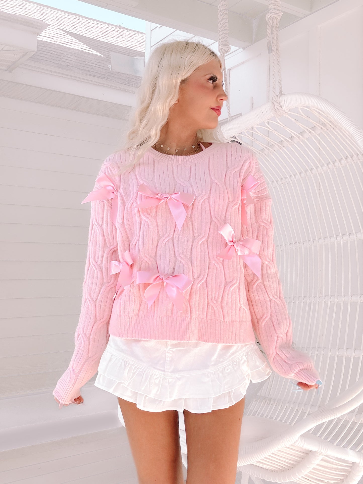 Light pink cable knit sweater adorned with satin bows, modeled outdoors.