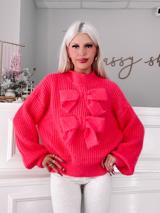 Hot pink knit sweater featuring oversized bows, modeled against a white backdrop.