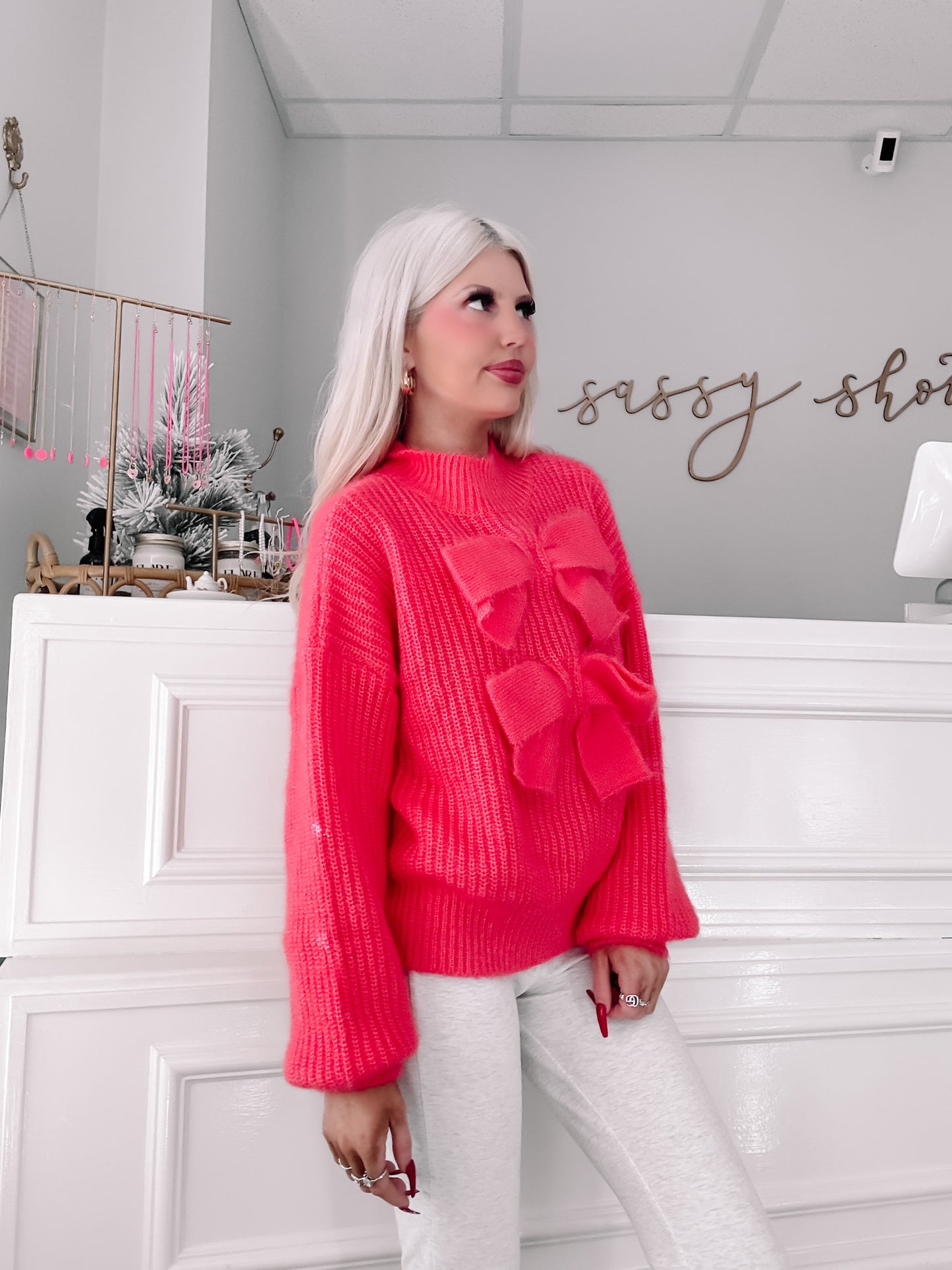 Hot pink knit sweater featuring oversized bows, modeled against a white wall.