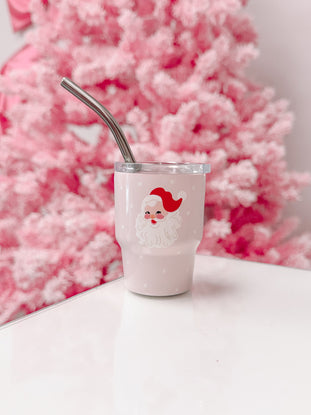 Pink Santa tumbler with metal straw, on white surface against a pink Christmas tree.