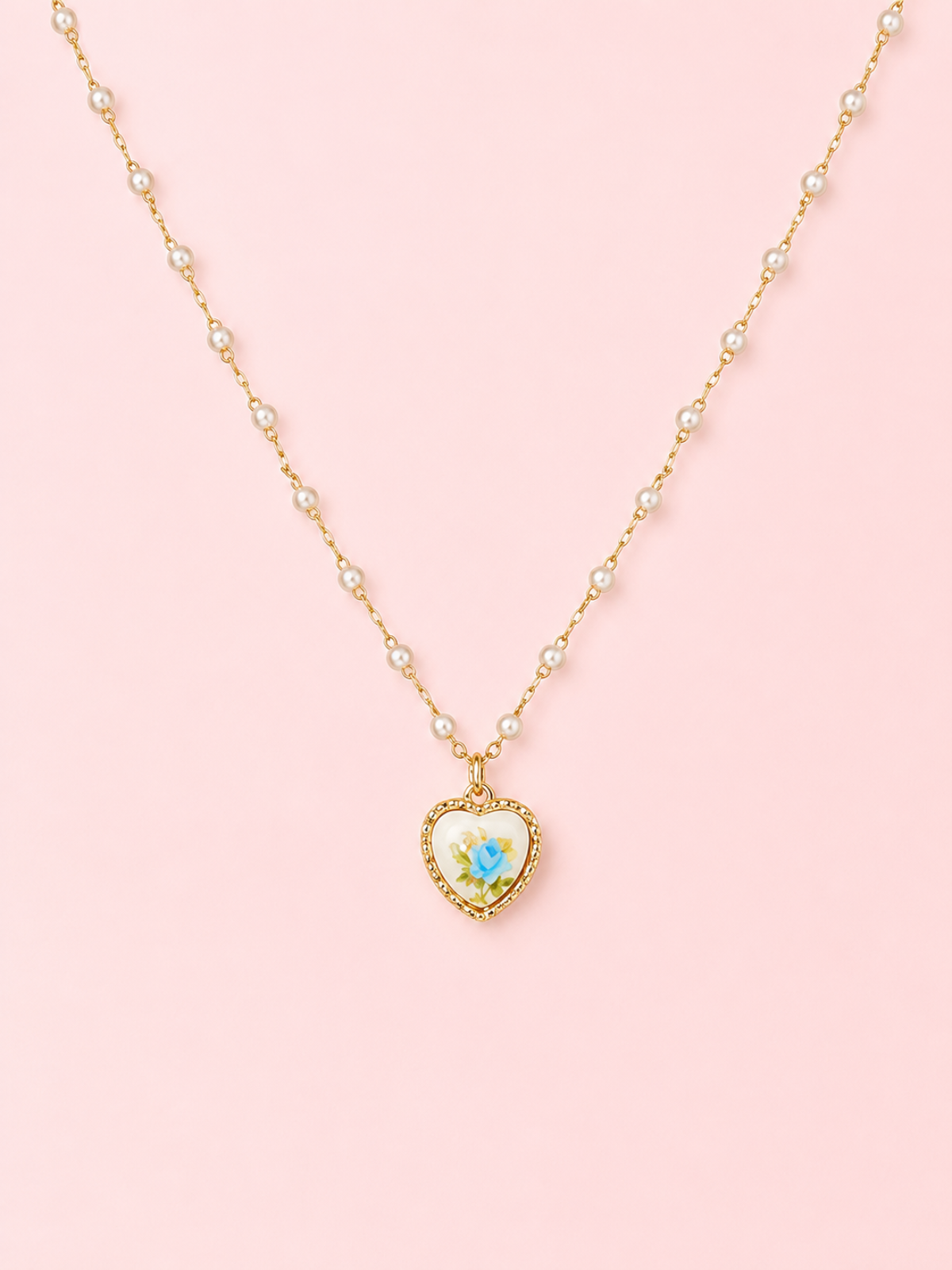 Sweet Bloom Bow Necklace in Blue from Sassy Shortcake featuring a gold-tone pearl-accent chain with a heart charm and blue rose print on a light pink background.