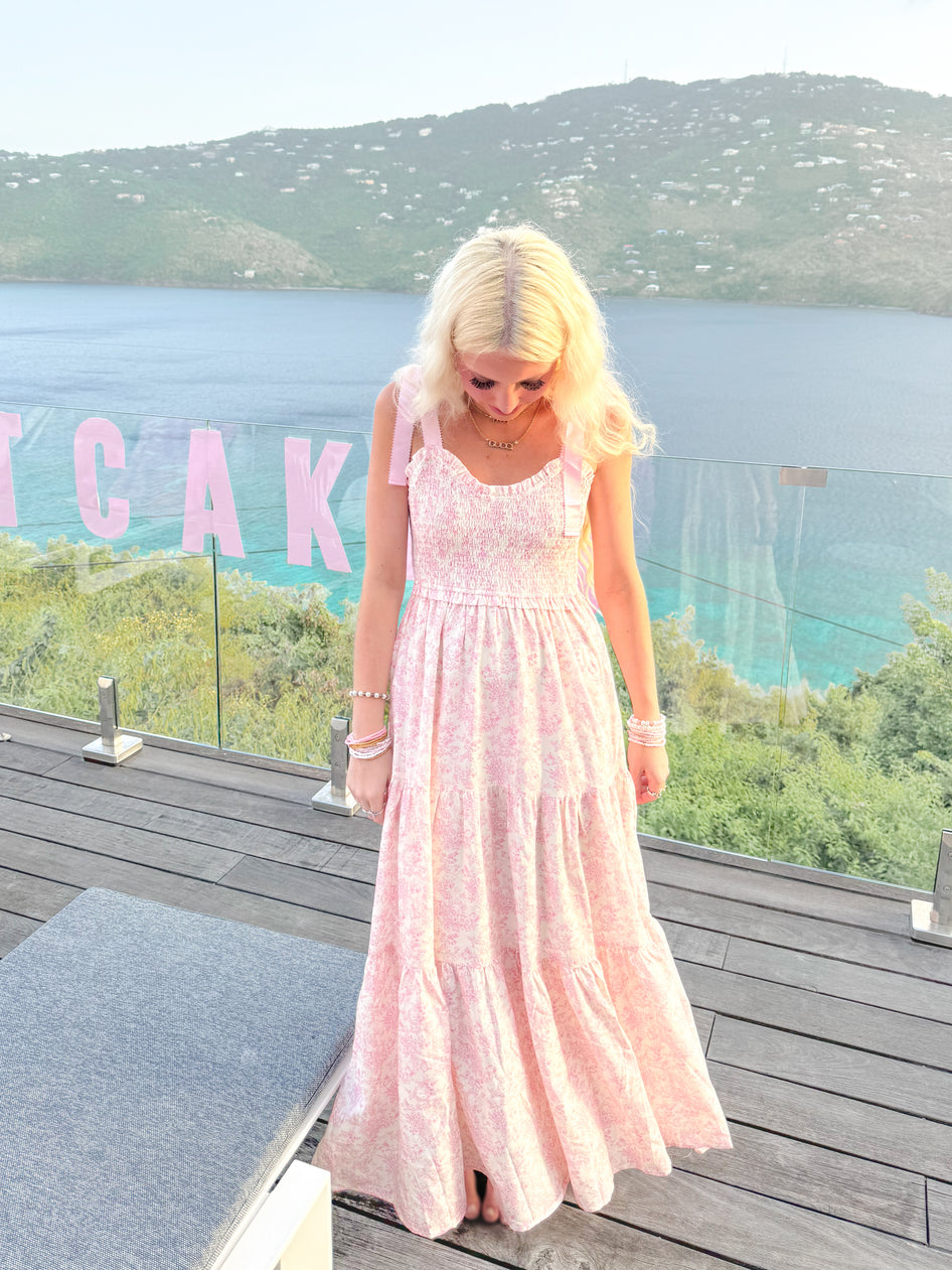 Back view of Sassy Shortcake Sweet Pea pink floral maxi; tie-shoulder straps and flowing tiered skirt on coastal deck in Virgin Islands