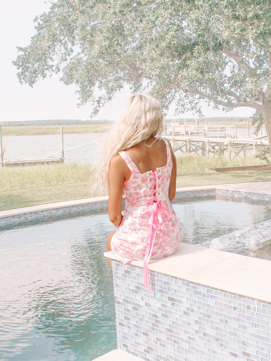 Pink toile print dress by the pool, featuring a corset back detail.