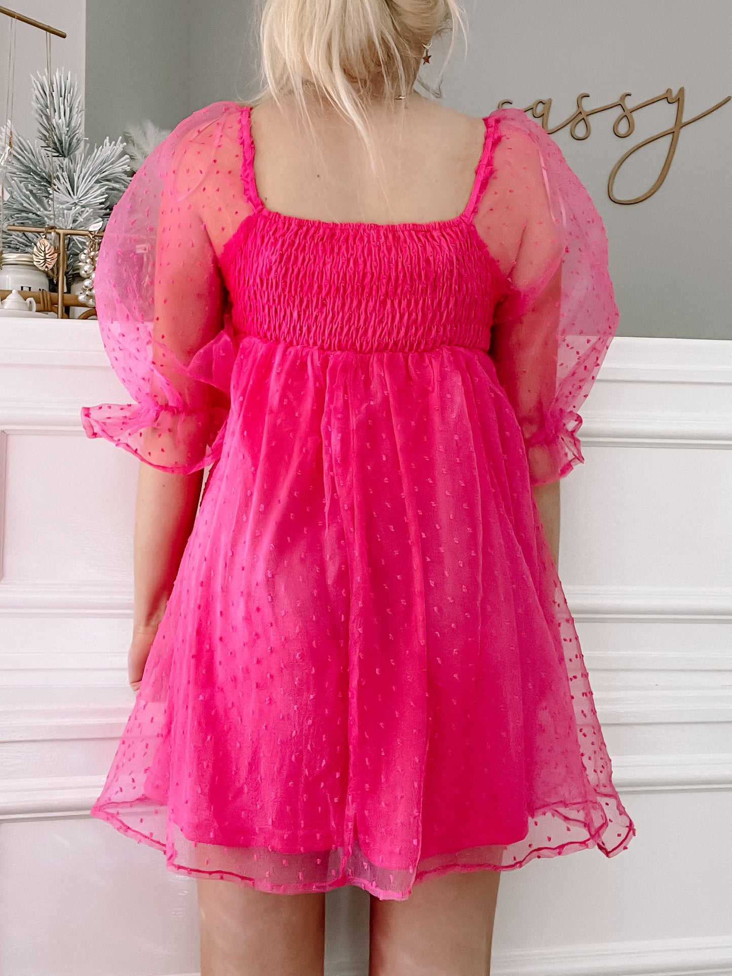 Hot pink tulle dress with puff sleeves, shown from the back against a white wall.