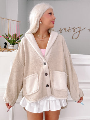 Cream-colored teddy fleece cardigan with contrasting trim and patch pockets, modeled against a light green wall.