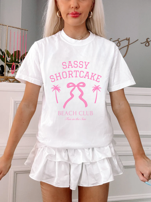 Model front-facing in white bow tee, bright pink graphic pops against white backdrop.