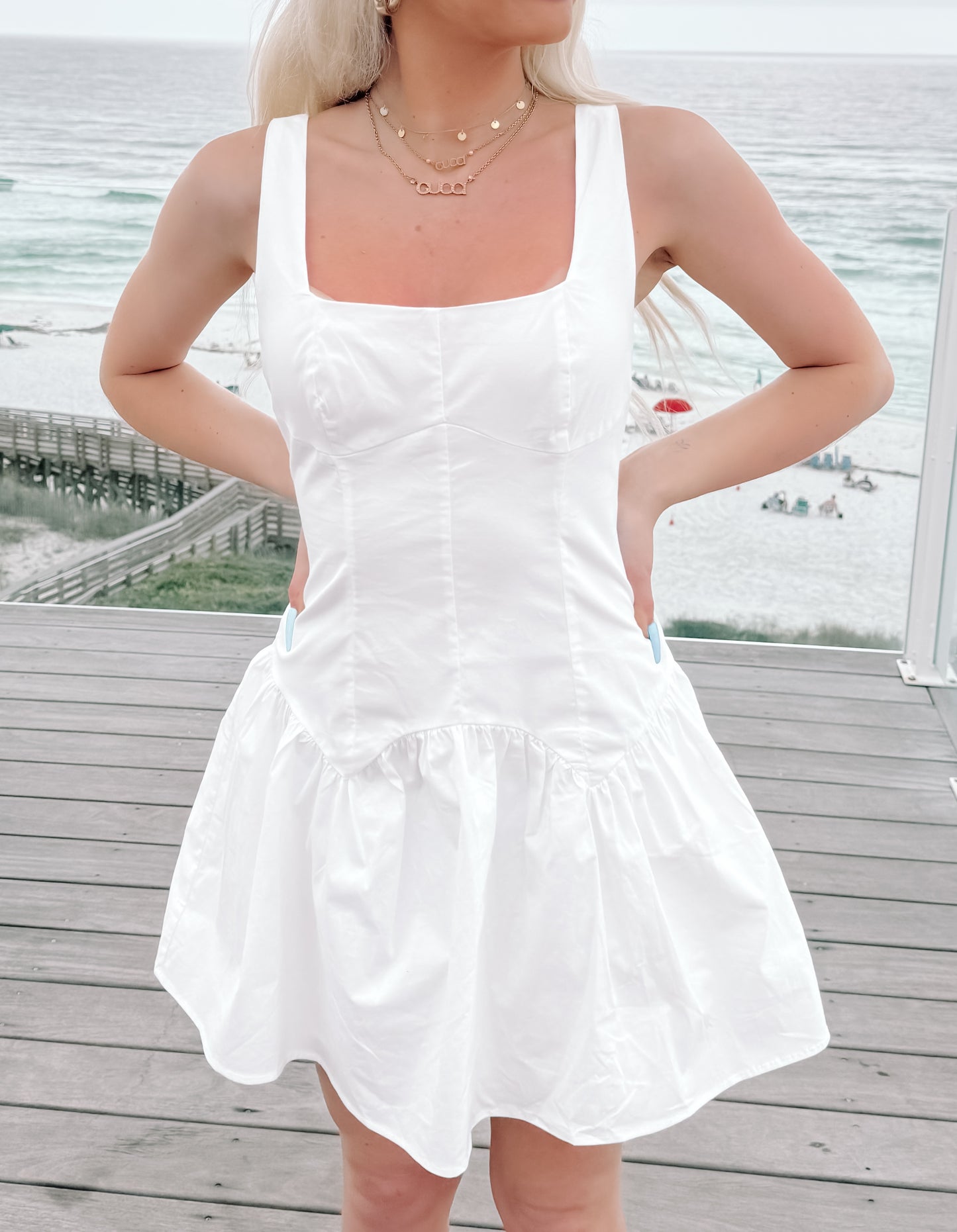 White summer dress with a ruffled hem, worn outdoors near the ocean.