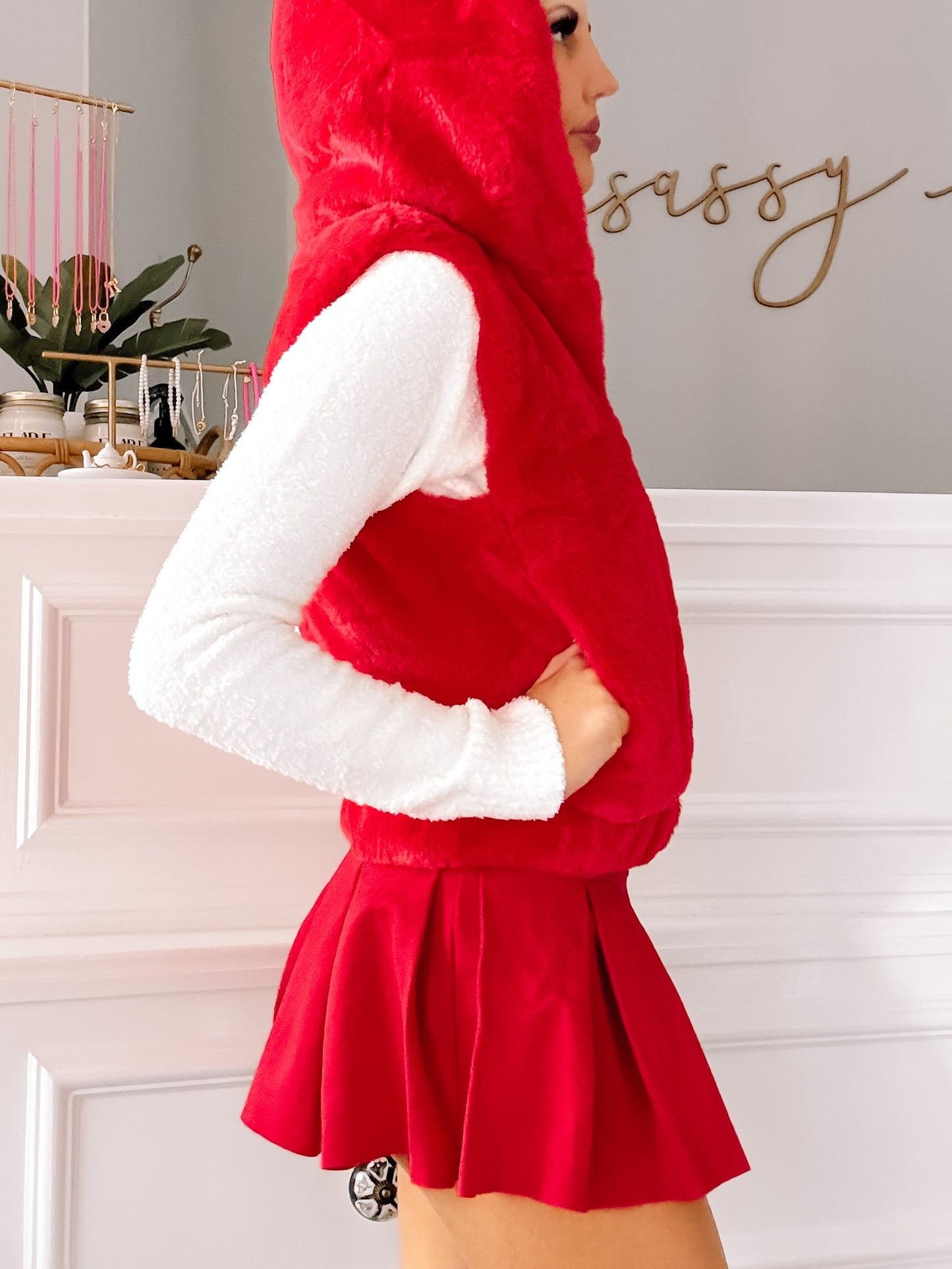 Red hooded faux fur vest styled with a white top and red pleated mini skirt.