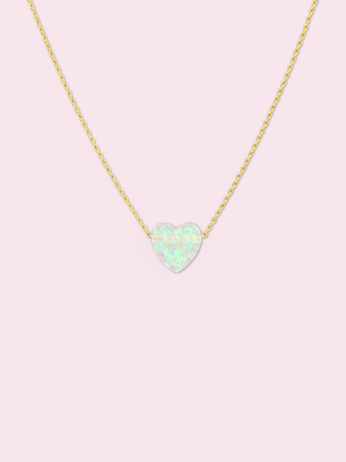 Dainty gold chain necklace featuring a pale opal heart pendant against a light pink backdrop.