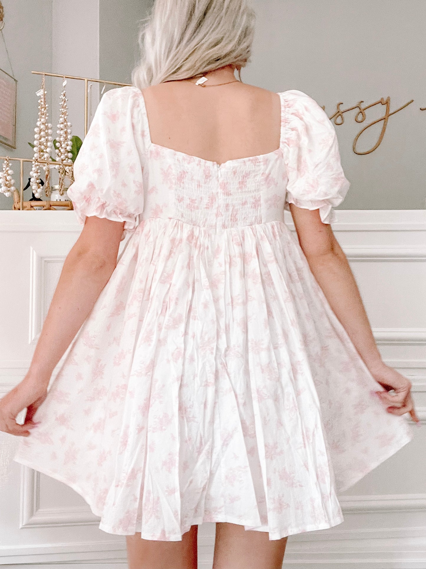 Pink floral mini dress with puff sleeves, shown from the back in a bright room.