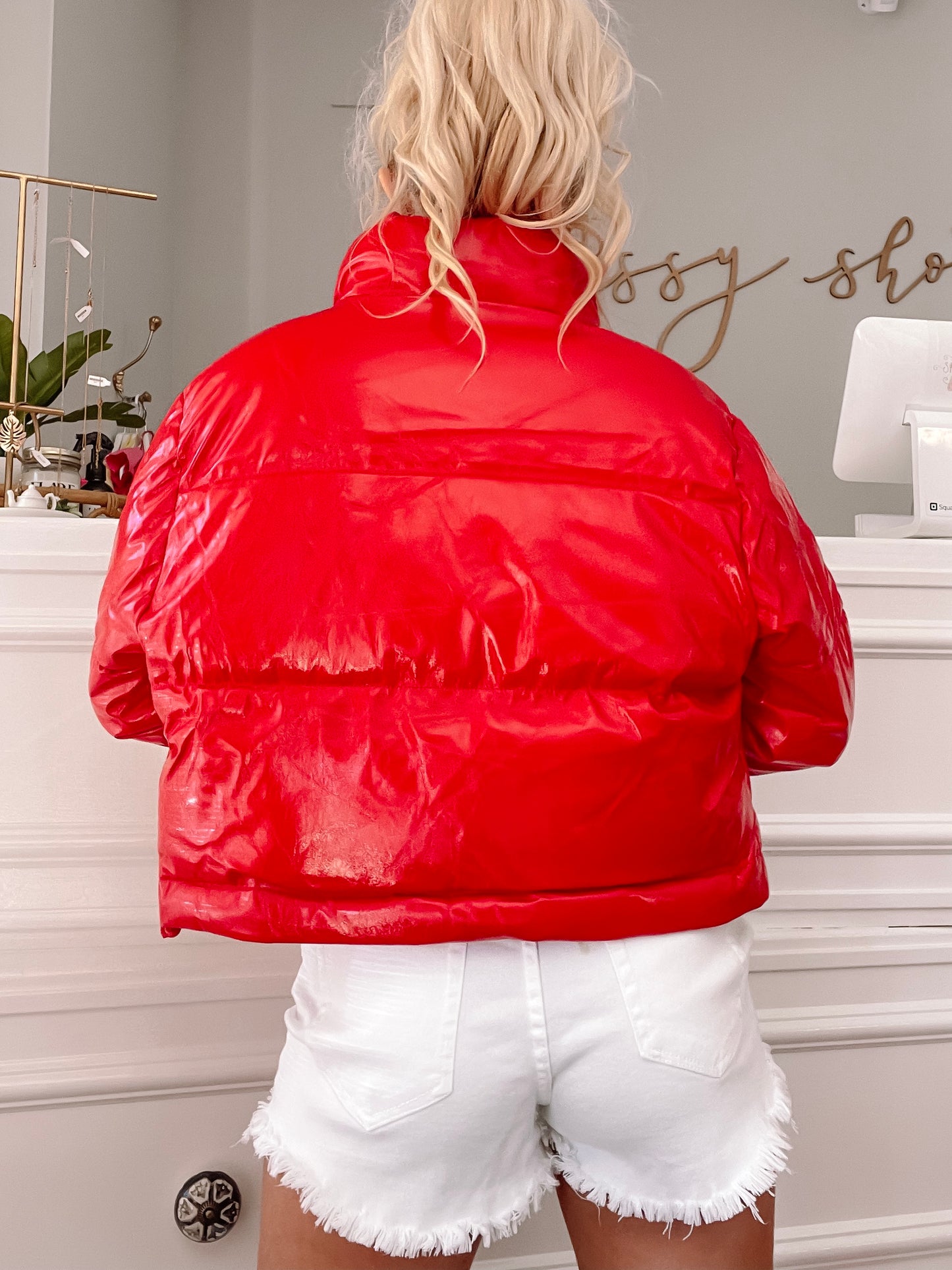 Shiny red puffer jacket, cropped view showcasing the back, in a bright shop setting.