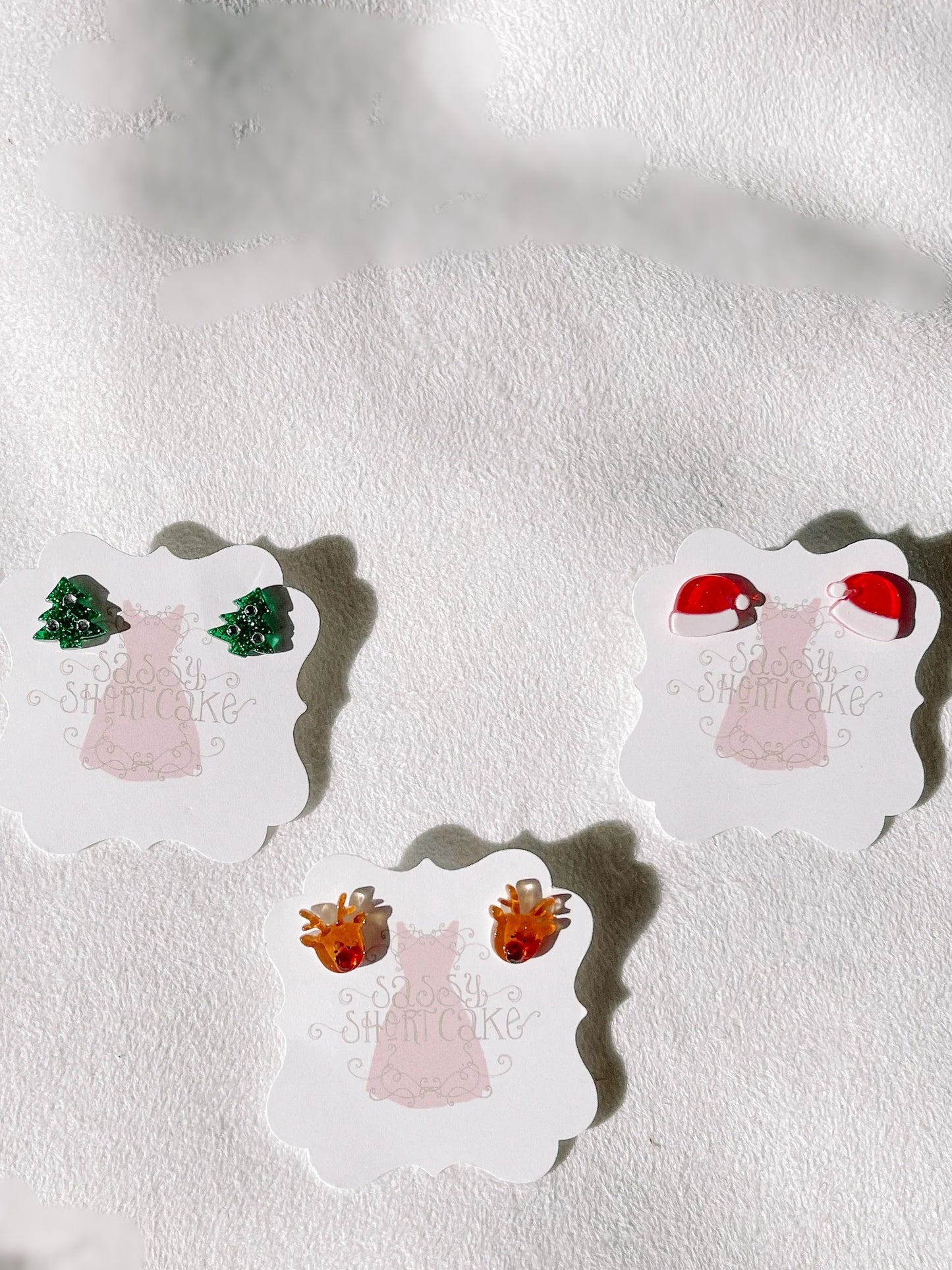 Miniature festive earrings displayed on cards; Christmas trees, Santa hats, and reindeer designs.
