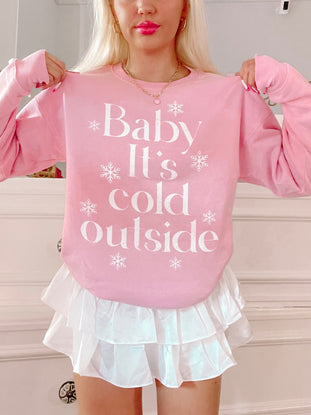 Pink crewneck sweatshirt with "Baby It's Cold Outside" text and snowflake accents, modeled with white skirt.