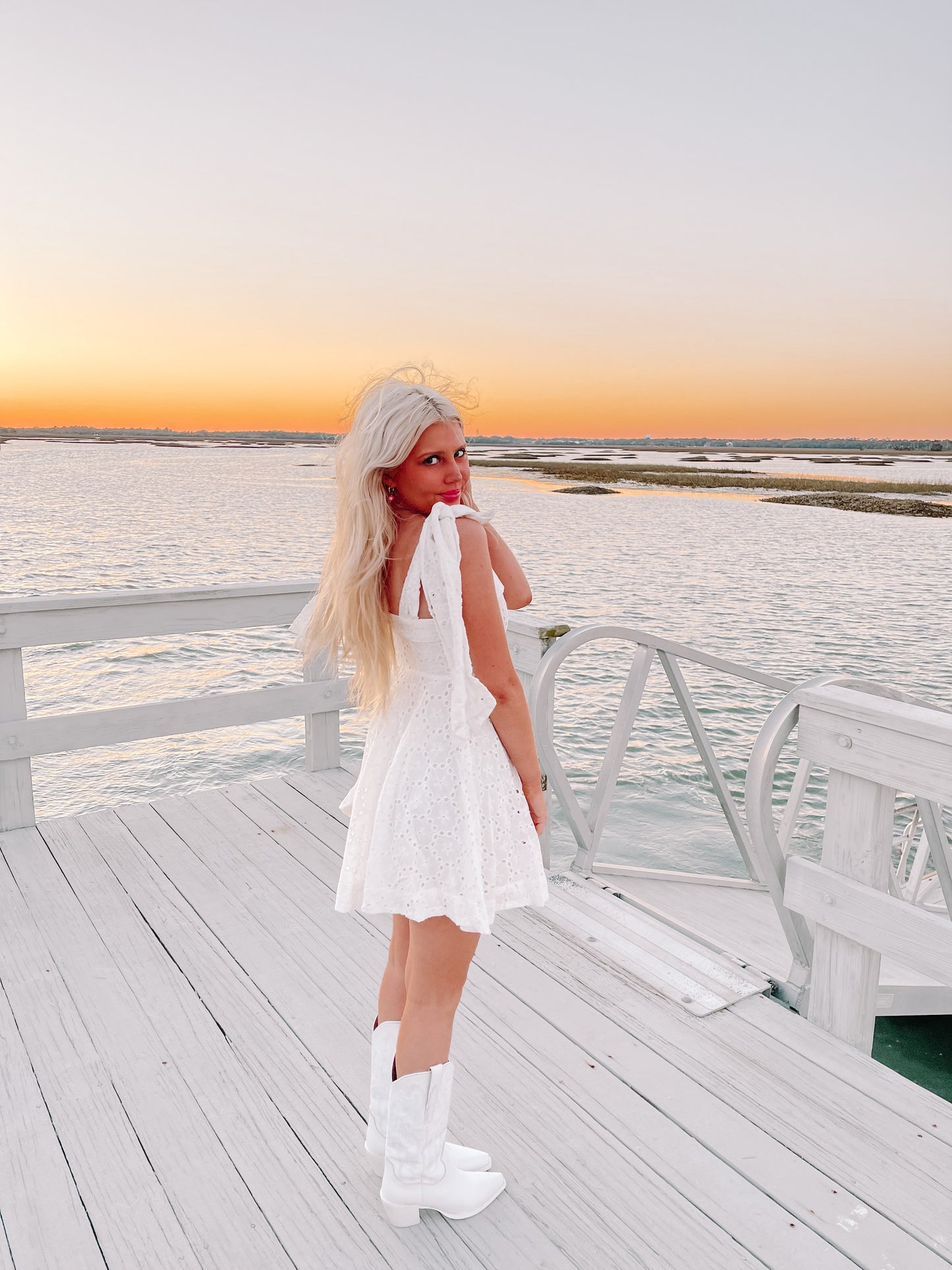 White eyelet dress on a dock at sunset, paired with white cowboy boots.