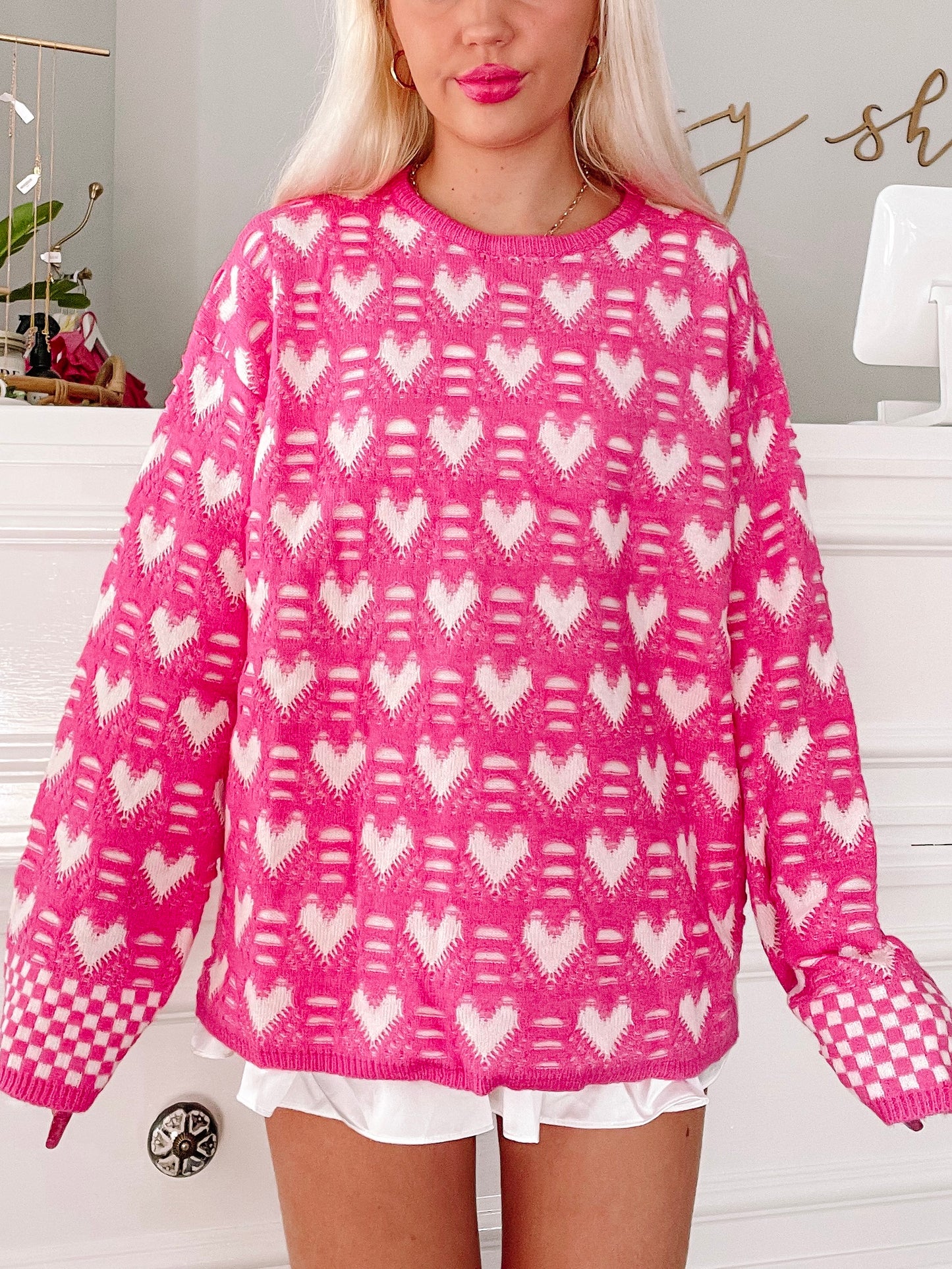 Pink sweater featuring a white heart pattern, shown on a model.