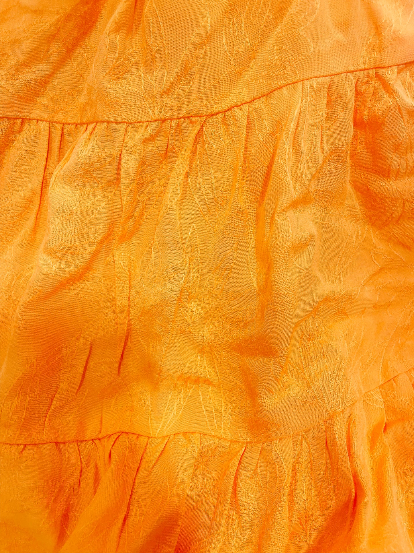Close-up of tangerine dress fabric with subtle textured pattern.