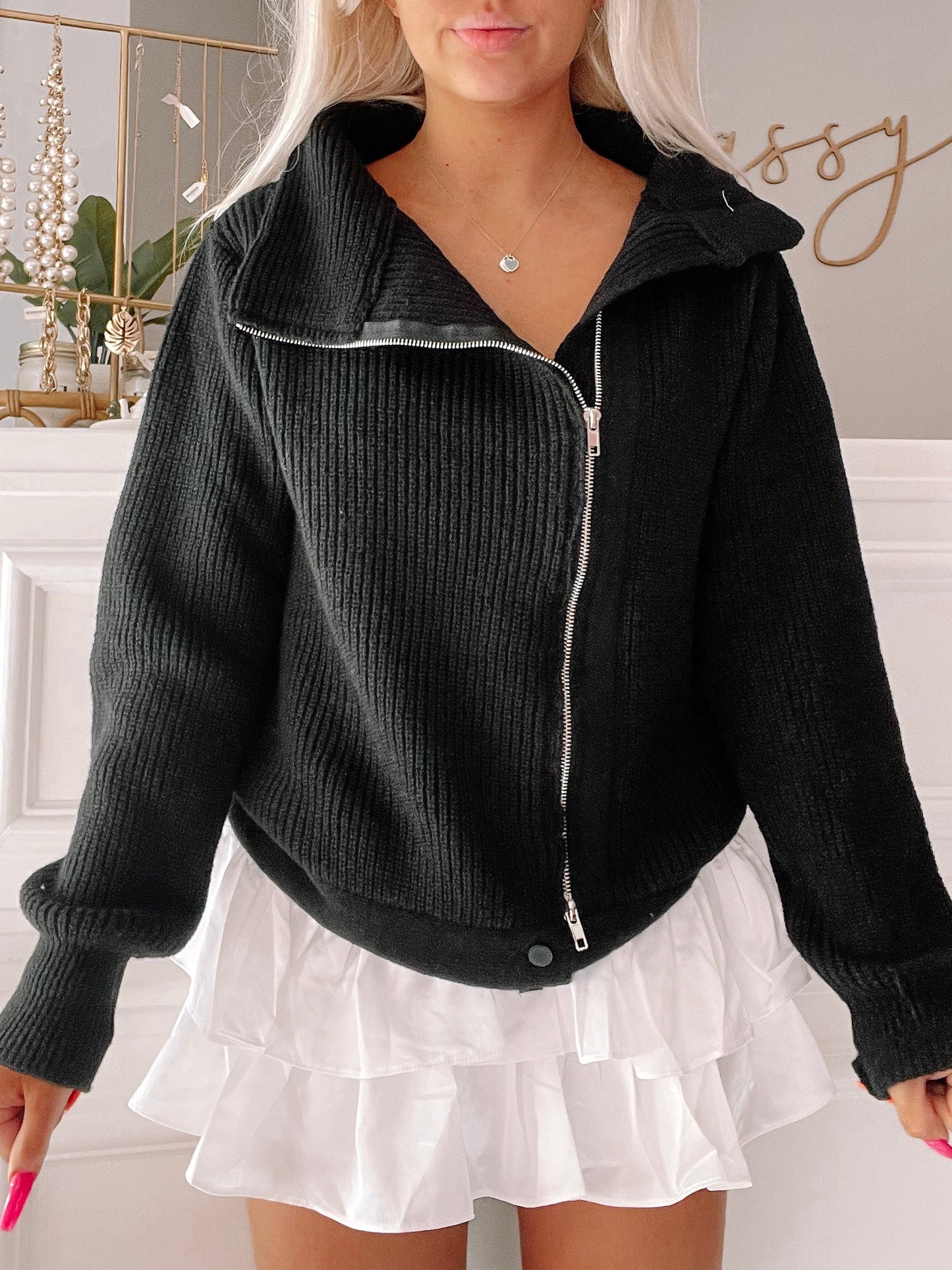 Black ribbed knit zip-up jacket styled with a white ruffled mini skirt.