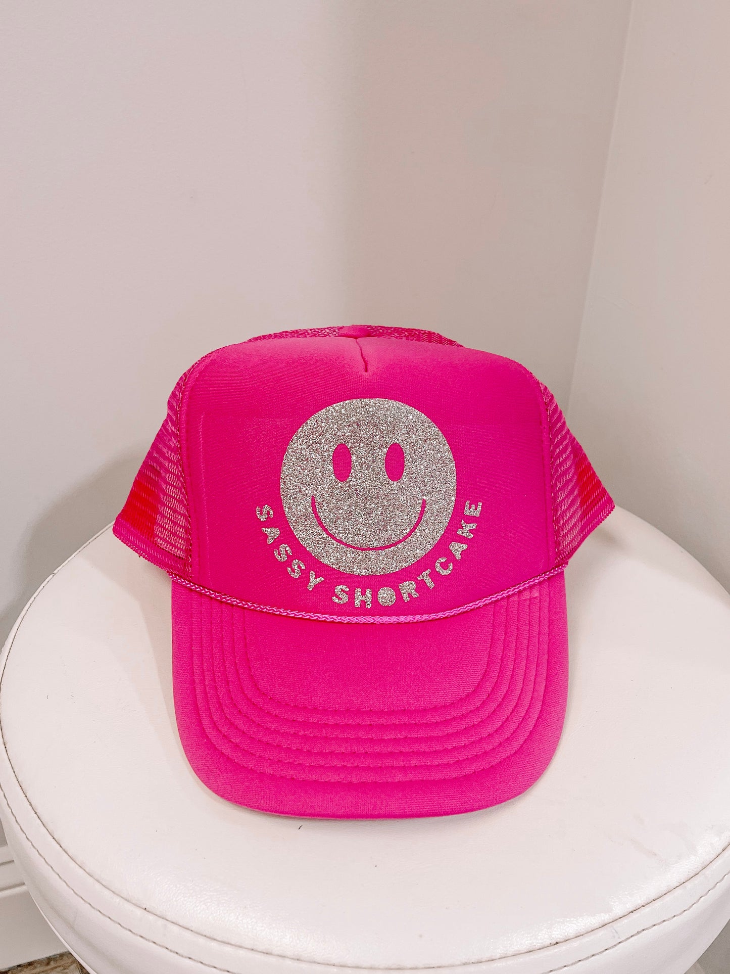 Pink trucker hat with silver glitter smiley face and text.