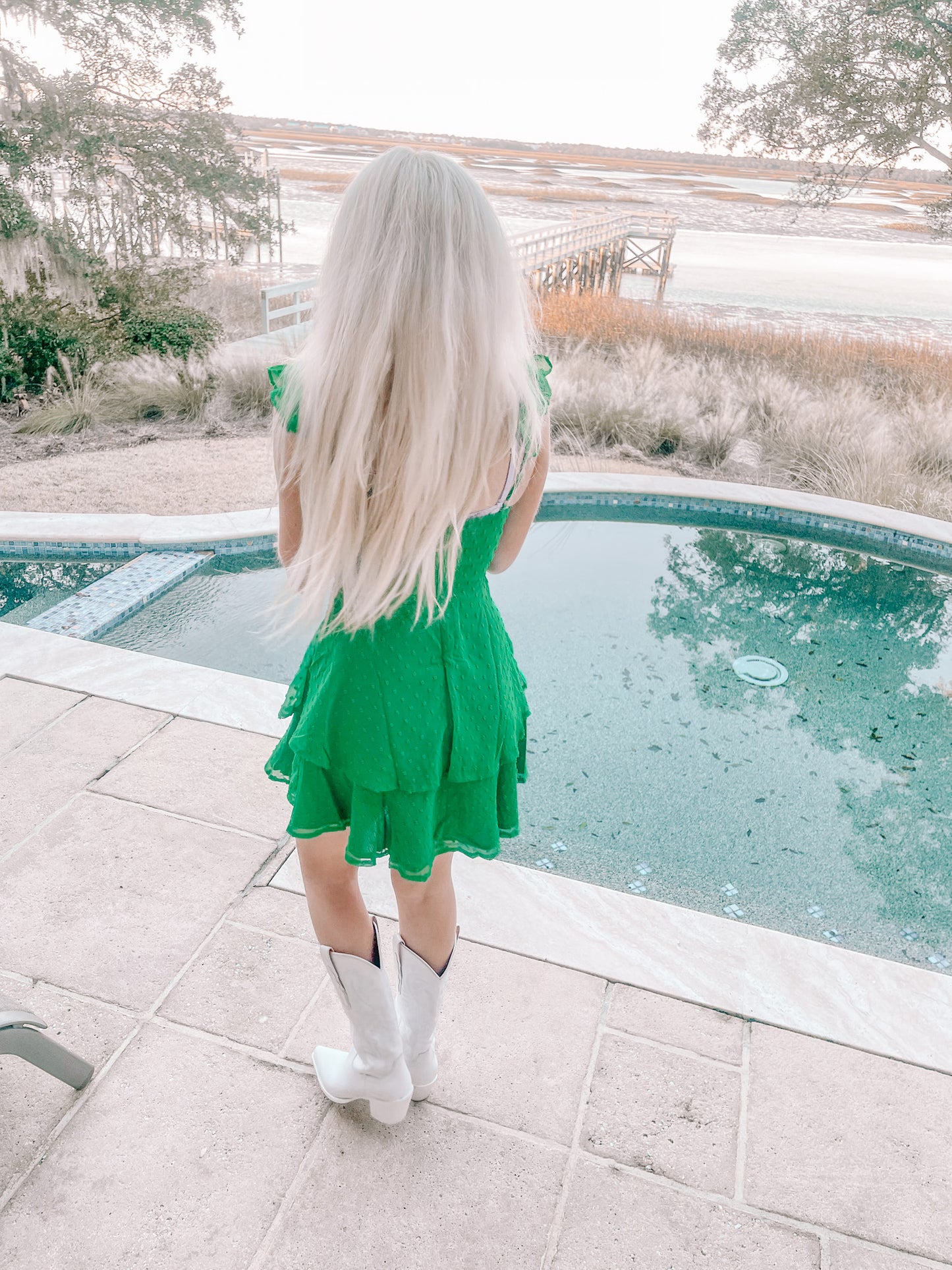 Woman in kelly green dress by pool, overlooking tranquil waterfront scene.
