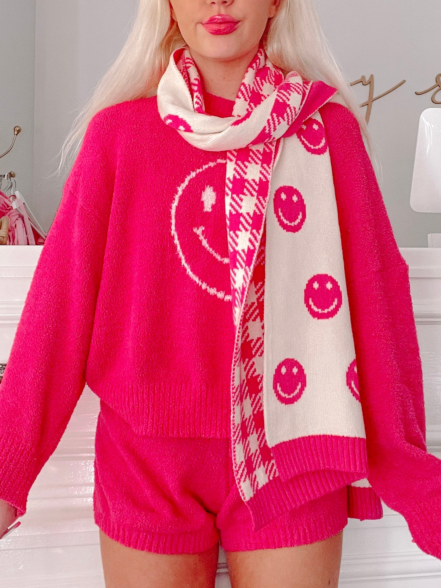 Cream and hot pink knit scarf with smiley face and houndstooth pattern, worn over a matching sweater.