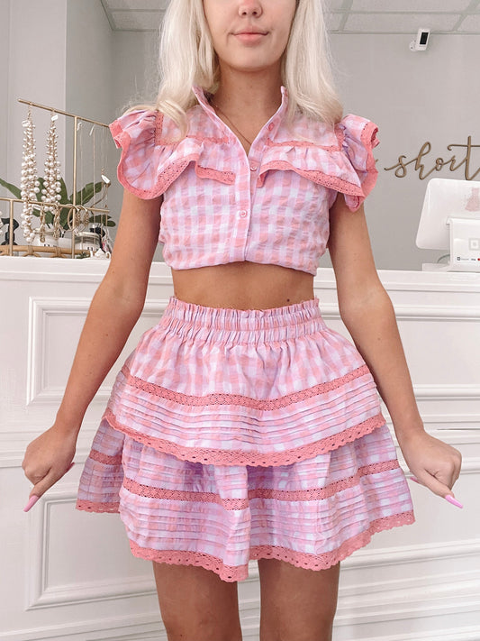 Pink gingham mini skirt with tiered ruffles and delicate lace trim, shown on a model.