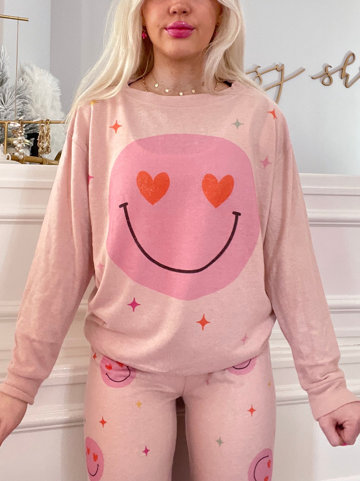 Pink pajama set featuring a smiley face design; long sleeves and pants with playful hearts and stars.
