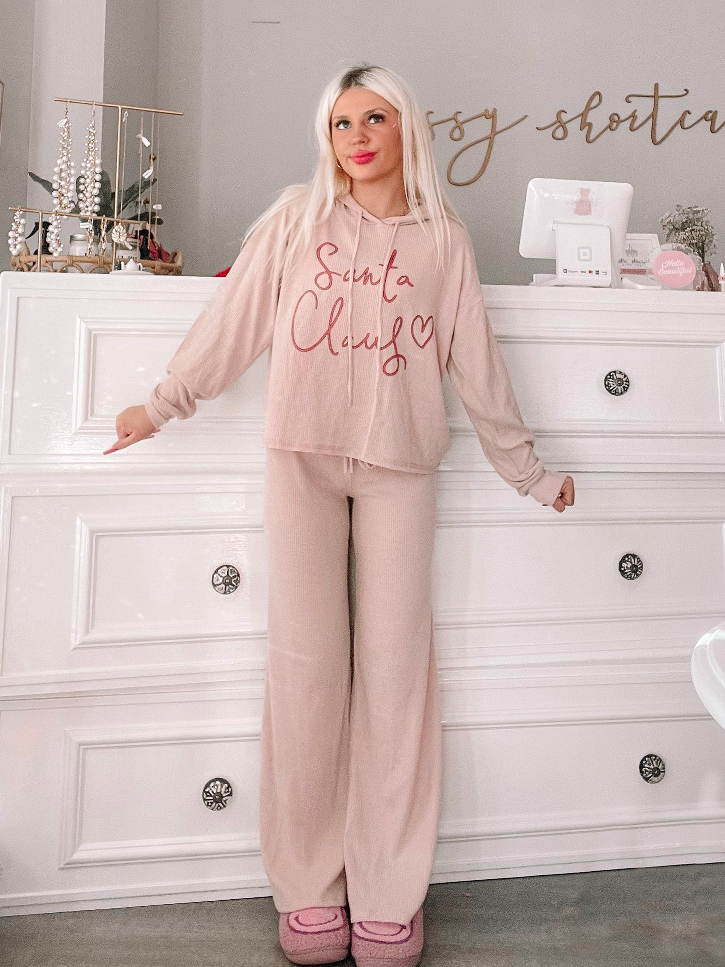 Cozy blush pink Christmas pajamas with a "Santa Claus" graphic, modeled against a white dresser.
