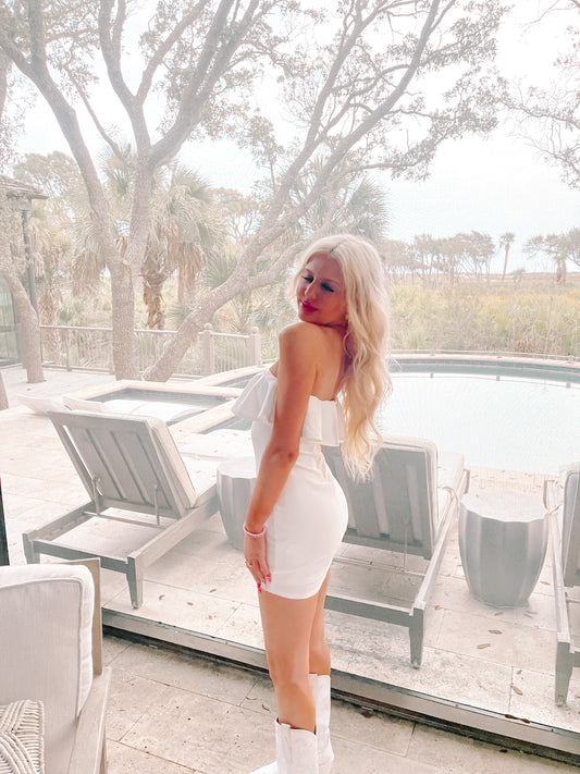 White ruffle mini dress, showcased near a poolside patio with lush greenery.