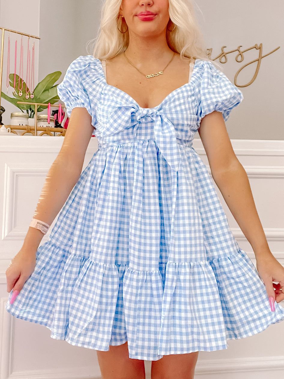 Blue gingham mini dress with puff sleeves and a bow detail, tiered skirt, shown on a model.