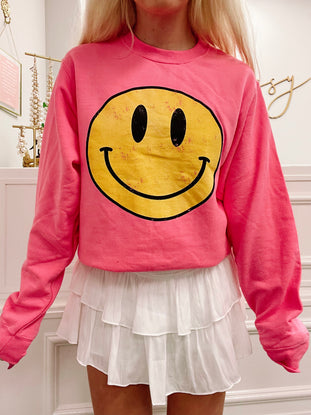 Pink sweatshirt featuring a vintage-style yellow smiley face graphic.