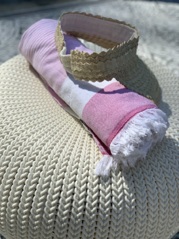 Straw visor and pink striped beach towel resting on a textured cream-colored surface.
