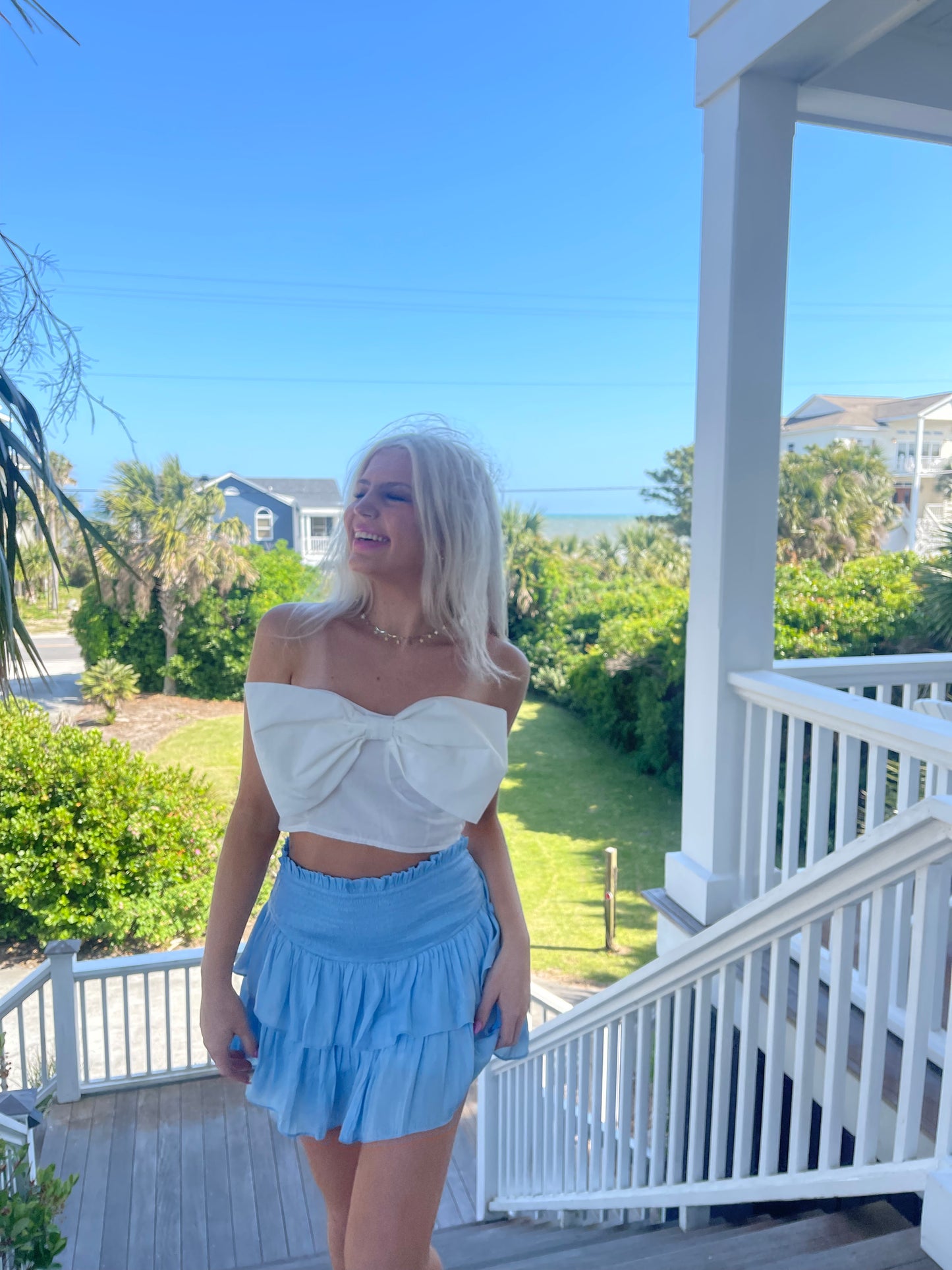 Light blue tiered mini skirt worn outdoors on a porch overlooking ocean view.