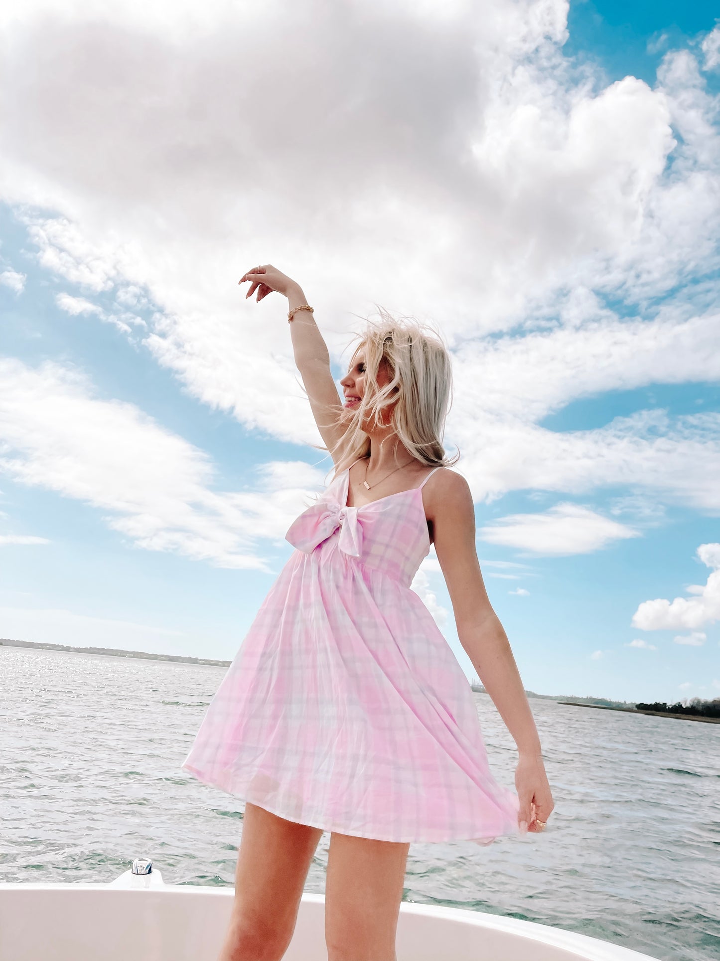 Pink and white gingham mini dress worn outdoors on a boat, under a bright summer sky.