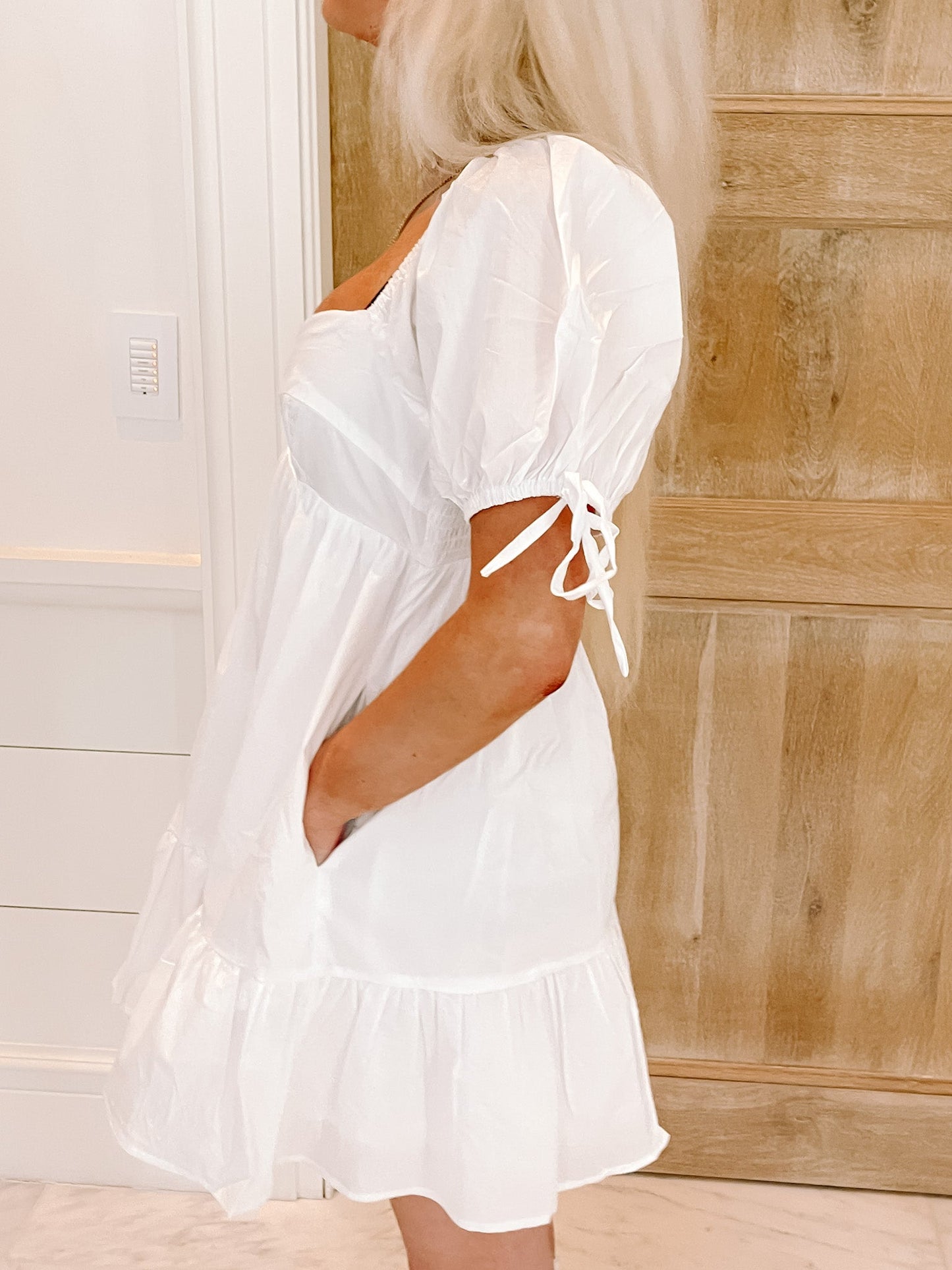 White puff-sleeve mini dress with tiered ruffle hem, shown against a light wood background.