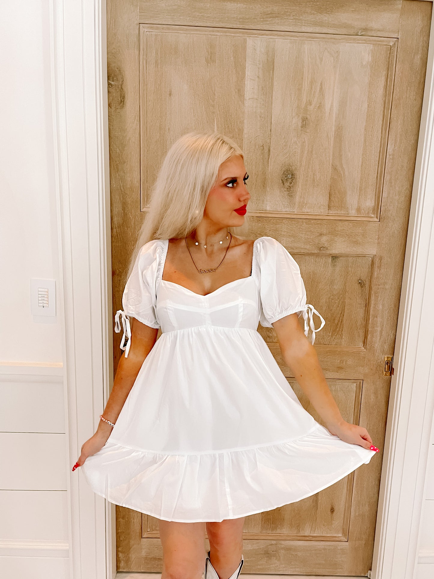 White puff-sleeve mini dress with tiered skirt, shown on model against light wood door.