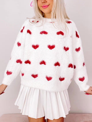 Fuzzy white sweater adorned with small red hearts; styled with a white pleated skirt.