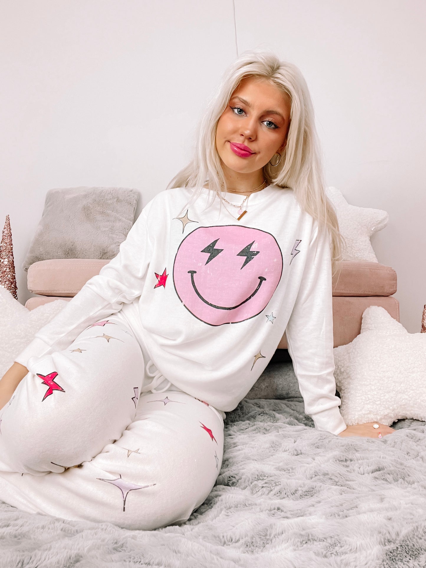 White pajama set with a smiling face and star design, modeled on a fluffy bed.