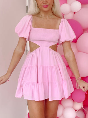 Pink mini dress with puff sleeves and cut-out detail, shown against a pink balloon backdrop.