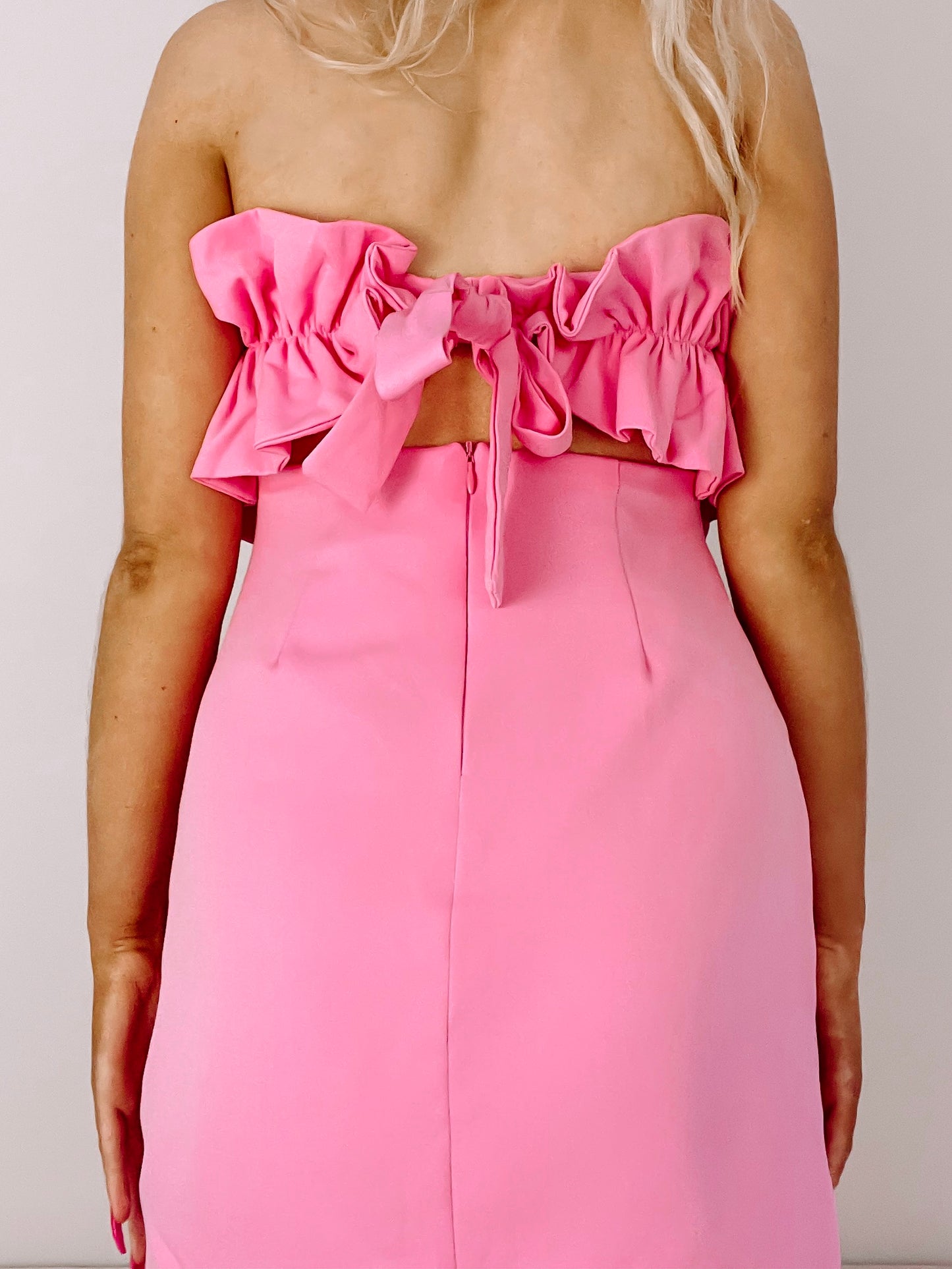 Pink mini dress with ruffled bodice and tie back detail.