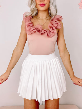 Dusty rose ruffle bodysuit paired with a white pleated mini skirt.