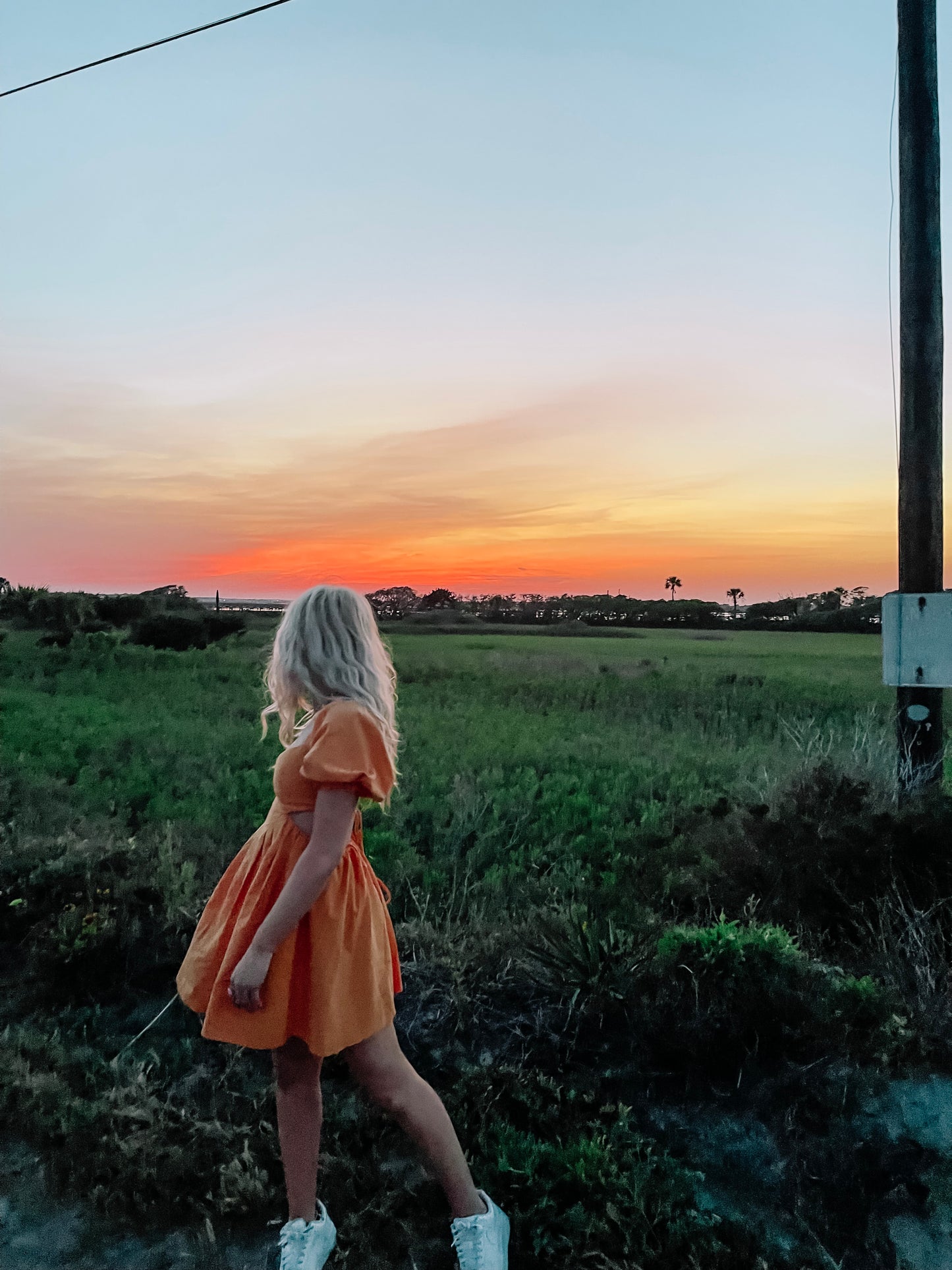 Woman in orange sundress at sunset, enjoying a scenic outdoor view.