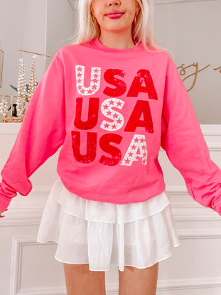 Hot pink sweatshirt featuring a red "USA" graphic with white stars, modeled indoors.