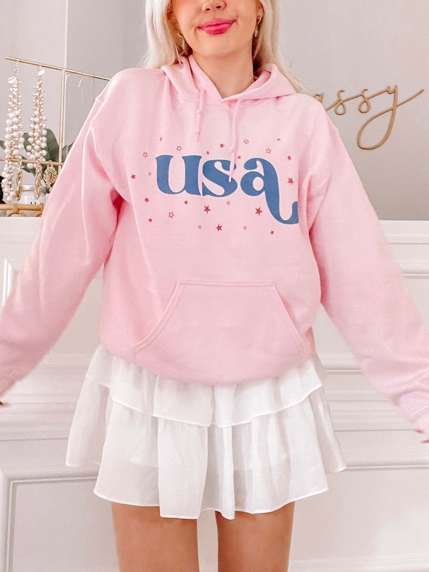 Pink hoodie featuring a retro "USA" graphic and scattered stars, modeled with a white tiered skirt.